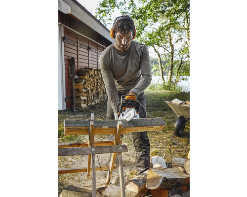 Mann sägt Holz mit einer Kettensäge auf einem Holzbock im Freien