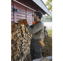 Mann stapelt Brennholz an einer Holzwand neben einem Haus.