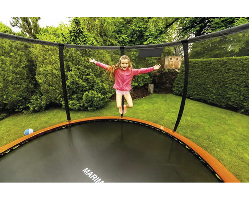Mädchen springt auf Gartentrampolin mit Sicherheitsnetz