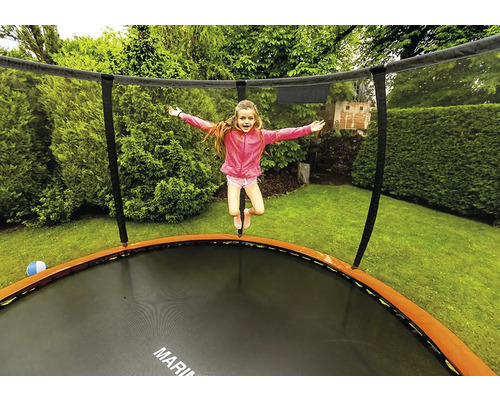 Mädchen springt auf Gartentrampolin mit Sicherheitsnetz