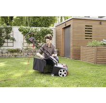 Eine Frau befestigt den Fangkorb an einem elektrischen Rasenlüfter im Garten.