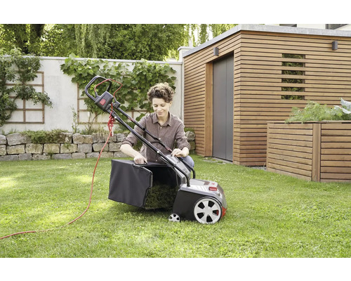 Eine Frau befestigt den Fangkorb an einem elektrischen Rasenlüfter im Garten.