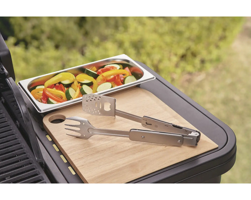 Gemüse in einer Schale, Grillzange und Schneidebrett auf einem Grill