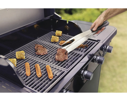 Grill mit Grillgut wie Steaks, Würstchen und Maiskolben, bedient mit Grillzange.