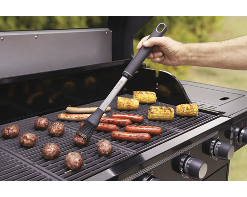 Grillszene mit Grillbürste, Würstel, Maiskolben und Fleischbällchen auf einem Gasgrill.