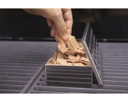 Befüllen einer Räucherbox mit Räucherchips auf einem Grill