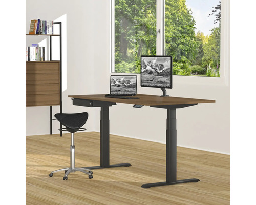 Höhenverstellbarer Schreibtisch mit Computern, Monitor und Sattelstuhl in einem hellen Raum.