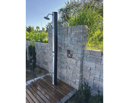 Gartenszene mit Außendusche aus Metall auf Holzdeck vor Steinmauer