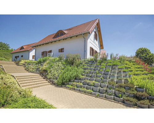 Haus mit Hangbefestigung aus Beton-Pflanzsteinen, Treppe und gepflastertem Weg.