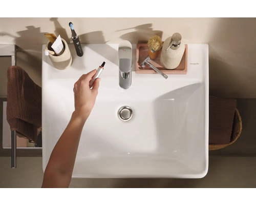 Draufsicht auf ein Badezimmerwaschbecken mit Armatur und diversen Badutensilien, eine Hand hält einen Nasenhaartrimmer.