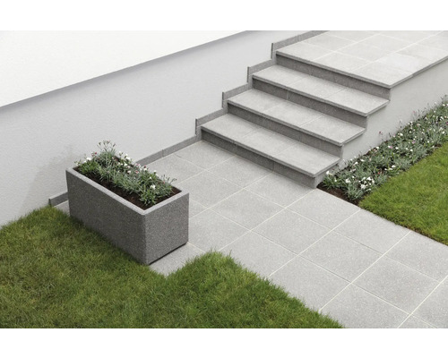 Außenbereich mit grauen Fliesen, Treppe und bepflanztem Blumenkasten.