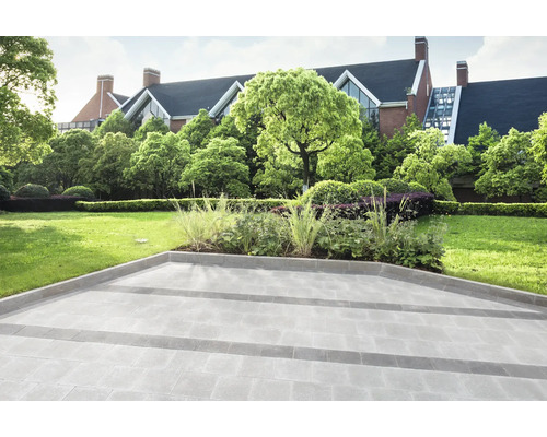 Gepflasterte Fläche mit Rasen und Gartenanlage im Hintergrund