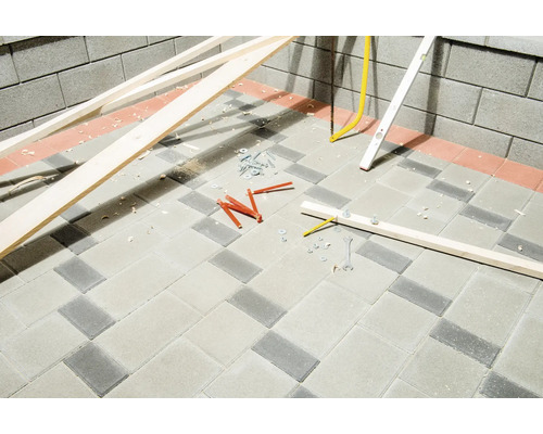 Baustelle mit Holzlatten, Wasserwaage, Dübeln und Schrauben auf Pflastersteinen