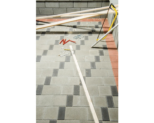 Baustelle mit Holzbalken, Handsäge, Schrauben, Dübel und Werkzeugen auf Pflastersteinen