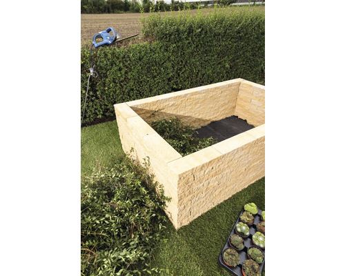 Beet aus Sandsteinquadern mit Pflanzenresten und Gartengeräten im Garten