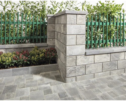 Gartenansicht mit einer Mauer aus Betonsteinen und einem grünen Zaun