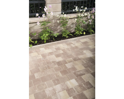 Gepflasterter Gartenweg mit Blumenbeeten entlang einer Steinmauer