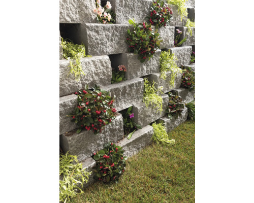 Gestapelte graue Pflanzsteine mit verschiedenen Pflanzen in einem Garten