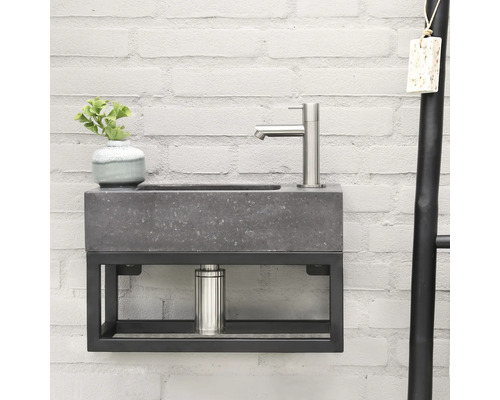 Modernes Waschbecken mit grauer Steinoptik und schwarzem Metallgestell an einer weißen Ziegelwand