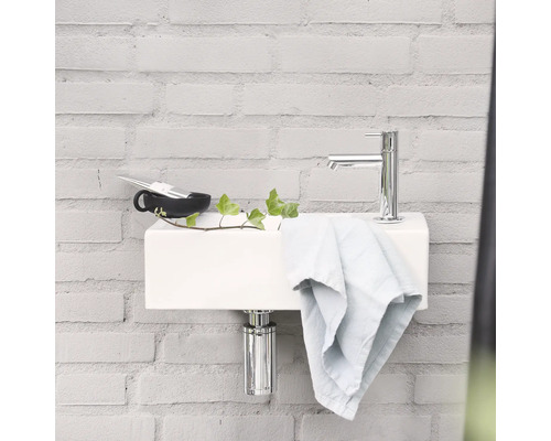 Modernes Badezimmer mit weißem Waschbecken, Chromarmatur und Handtuch vor einer Backsteinwand