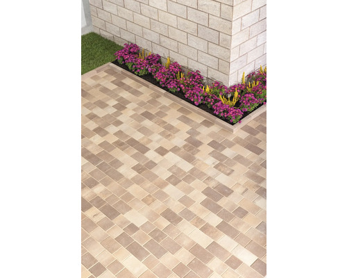 Verlegter Pflastersteinweg mit Blumenbeet an einer Hauswand.