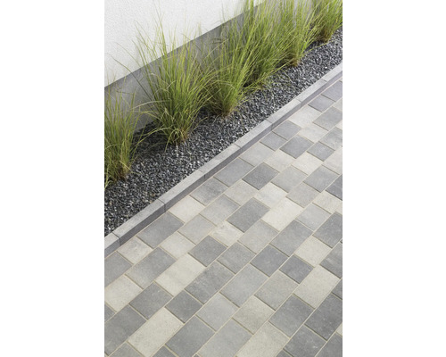 Pflastersteine aus Beton in Grau- und Weißtönen verlegt, angrenzend an Kies und Gras
