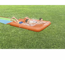 Zwei Kinder spielen auf einer aufblasbaren Wasserrutsche im Garten.