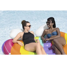 Zwei Frauen entspannen auf einer regenbogenfarbenen Pool-Luftmatratze im Wasser.