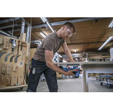 Ein Mann sägt mit einer Stichsäge ein Werkstück in einer Werkstatt.