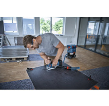 Ein Mann verwendet einen Schleifer mit Staubsauger an einer dunklen Platte in einem hellen Raum.