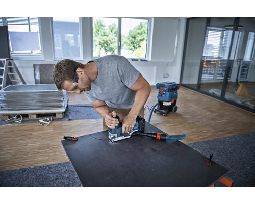 Ein Mann verwendet einen Schleifer mit Staubsauger an einer dunklen Platte in einem hellen Raum.