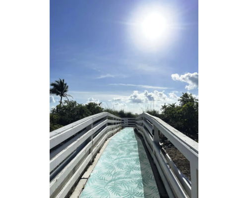 Holzsteg mit Muster auf dem Weg zum Strand unter blauem Himmel.
