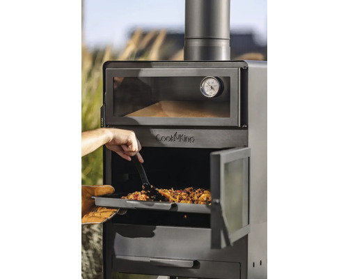 Ein Mann schiebt eine Mahlzeit mit einem Spatel in einen Outdoor-Ofen der Marke Cook King.