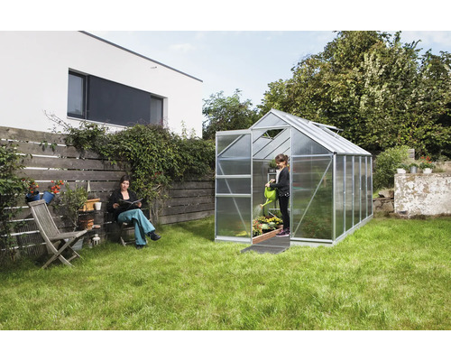 Gewächshaus im Garten mit Frau auf einem Stuhl und Mädchen beim Gießen von Pflanzen