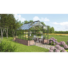 Gewächshaus mit Backsteinsockel, Glaswänden und einem Tisch mit Stühlen im Inneren in einem Garten.