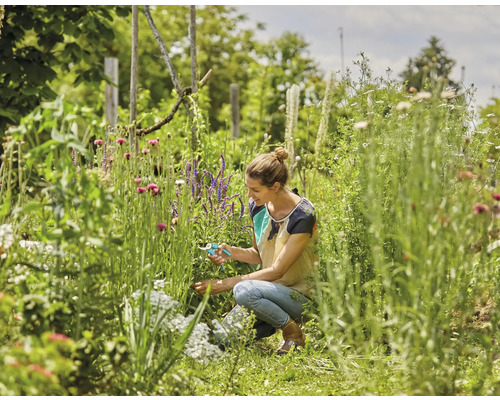 Eine Frau arbeitet mit einer Gartenschere in einem blühenden Garten.