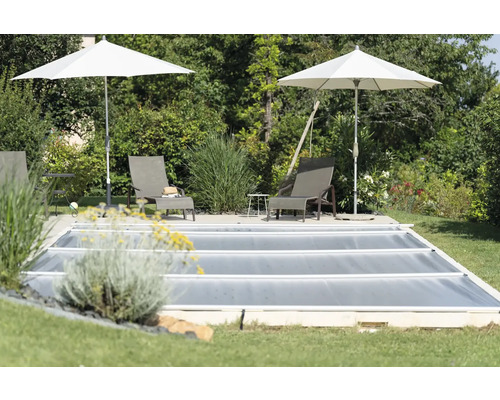 Abgedeckter Pool mit zwei Liegestühlen und Sonnenschirmen im Garten.