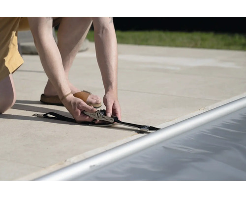 Person befestigt eine Poolabdeckung mit einem Spanngurt.