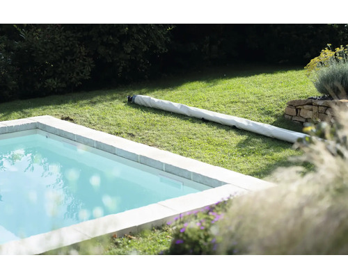 Aufnahme eines Schwimmbeckens im Garten mit aufgerollter Poolabdeckung auf dem Rasen
