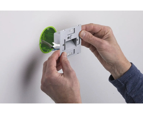 Ein Elektriker montiert einen Bewegungsmelder an einer Wand.