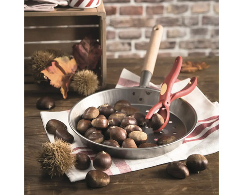 Esskastanien in einer Pfanne mit Kastanienzange auf einem Holztisch