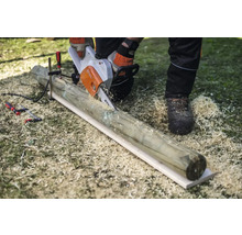 Eine Person sägt mit einer Motorsäge einen Holzpfosten, der mit einer Klemme fixiert ist.