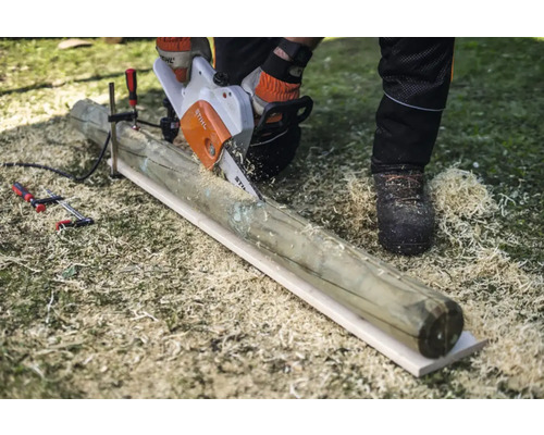 Eine Person sägt mit einer Motorsäge einen Holzpfosten, der mit einer Klemme fixiert ist.