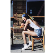 Eine Frau mit einem blauen Stirnband und gelbem Tuch sitzt auf einem Stuhl und trinkt ein Getränk.