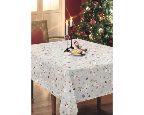 Festlich gedeckter Tisch mit Tischdecke mit Weihnachtsmuster, Kerzen und Weihnachtsbaum im Hintergrund.