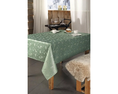 Esstisch mit grüner Tischdecke mit Hirsch- und Tannenbaum-Muster, gedeckt mit Geschirr, Getränken und Kuchen.