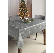 Festlich gedeckter Tisch mit grauer Tischdecke mit Hirschmotiven neben einem geschmückten Weihnachtsbaum.