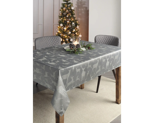 Festlich gedeckter Tisch mit grauer Tischdecke mit Hirschmotiven neben einem geschmückten Weihnachtsbaum.