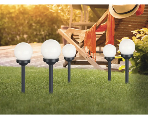 Mehrere Gartenkugelleuchten mit Erdspieß im Rasen vor einer Gartenszene.