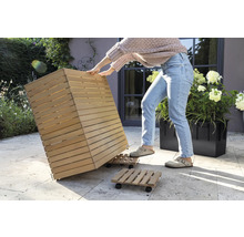 Eine Person bewegt einen Pflanzkübel aus Holz auf einem Rollbrett im Garten.